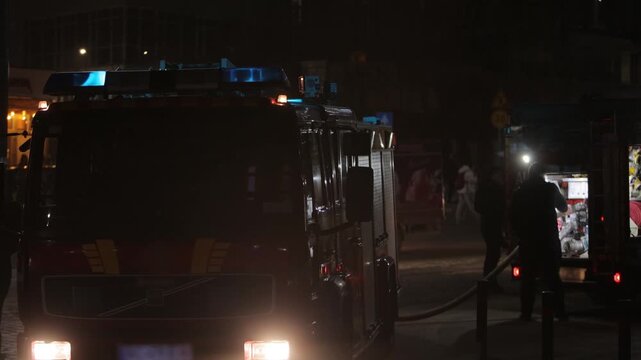 night emergency, fire trucks, blue lights. Night emergency scene with fire trucks, flashing blue lights, firefighters, and open equipment compartments during urban rescue response.