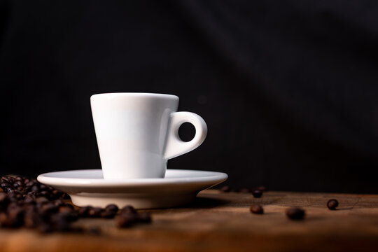 Wei&szlig;e Espressotasse auf Holztisch vor schwarzem Hintergrund