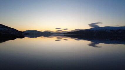 Fototapeta premium Calm Norwegian fjord at sunset with soft pastel sky and perfect mirror reflection on still water. Minimal Scandinavian landscape with large copy space for design use.