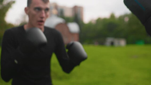urban shadowboxing solo training in park with guard up and crisp footwork, black gloves, distant buildings on skyline, green lawn surroundings, focused breathing and repetitive motion, defensive