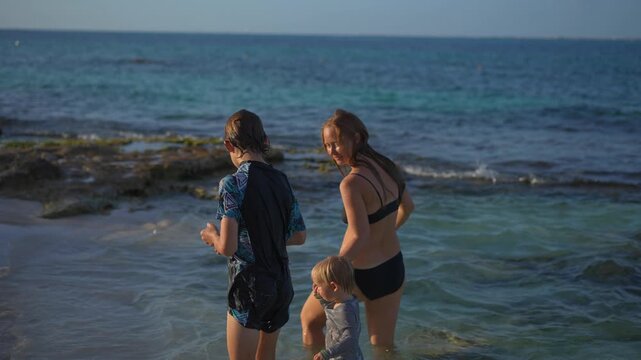 Young mom spending quality time with her two sons on a beautiful tropical beach, enjoying sunshine, laughter, and family bonding moments by the sea.