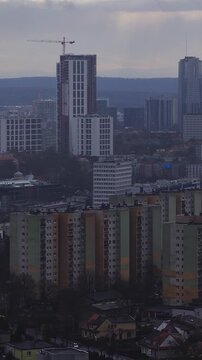 Aerial sweep over Katowice, Poland shows a crane topped high rise, modern office towers, prefabricated blocks, and houses under overcast late afternoon light.