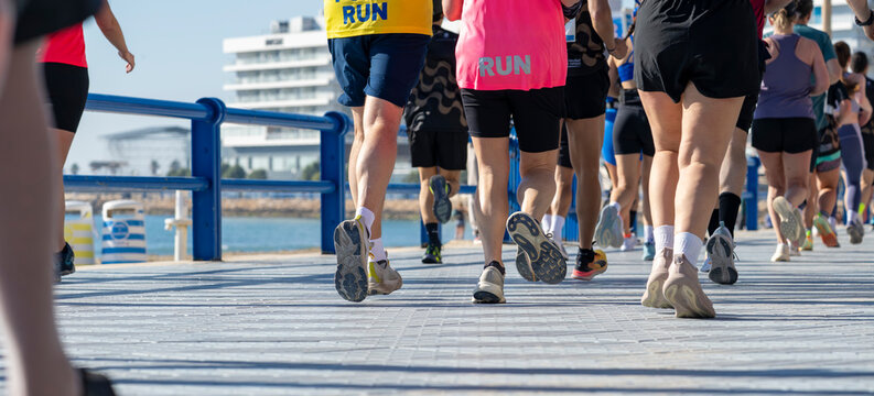 Marathon participants running beside blue railings on waterfront promenade