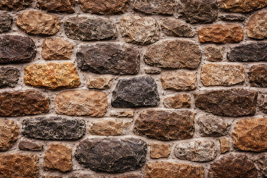 A detailed close up view of a rustic wall constructed from uneven natural brown fieldstone rocks