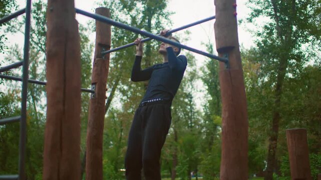 man training on outdoor pullup bar, wooded park setting with wooden posts and metal crossbar, repeated pull attempts, focused expression, slow controlled motion, black training kit, raw determination
