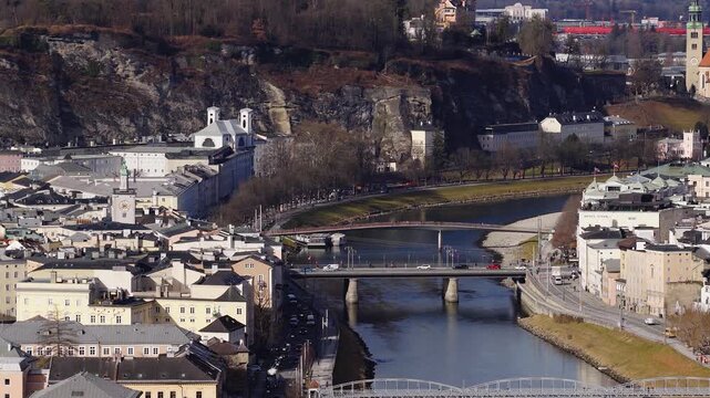 Aerial view of Salzburg, Austria shows the Salzach River, Monchsberg, Hotel Stein, baroque facades, bridges, cars and pedestrians in crisp daytime with deep shadows.