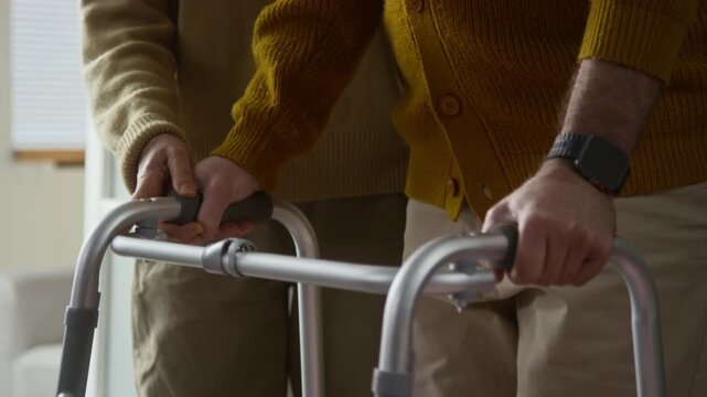 Tilt up view of senior woman assisting and encouraging her husband while he learning to walk using walking frame at home