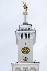 Naklejka premium Front view of historic clock tower topped by a Soviet golden star rises against a cloudy sky. The North River Terminal or Rechnoy Vokzal of Moscow, Russia. It was built in 1937