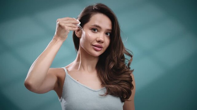 Female model using cosmetic serum dropper on facial skin in studio. Skincare concept.
