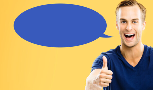 Portrait image - happy smile young man wear casual cloth shows points thumb up thumbup finger hand gesture, isolated orange yellow background. Blue empty speech bubble speechbubble. Right choice