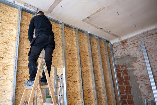 Builder Aligning Steel Stud Wall Frame Against OSB Panels in Renovation Room