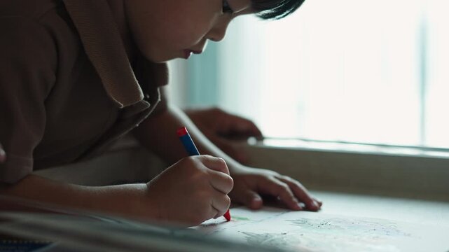 Focused young boy drawing with crayons, developing artistic skills indoors