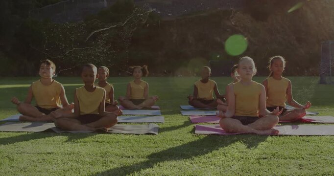 Teacher giving cue, eight kids meditating on yoga mats, sunlight making green lens flare for school