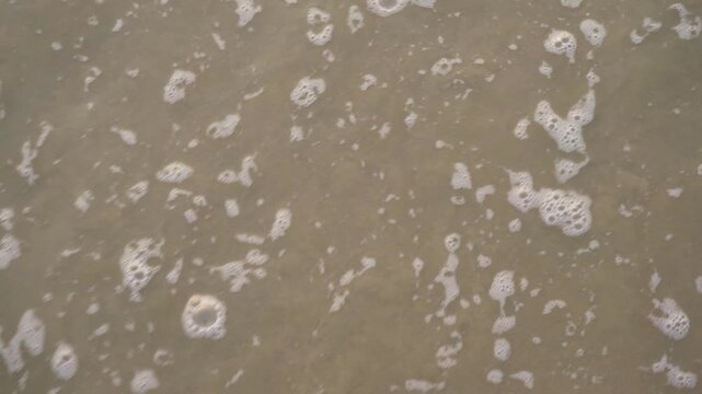 Top-down view of gentle ocean waves and white sea foam washing over wet beach sand