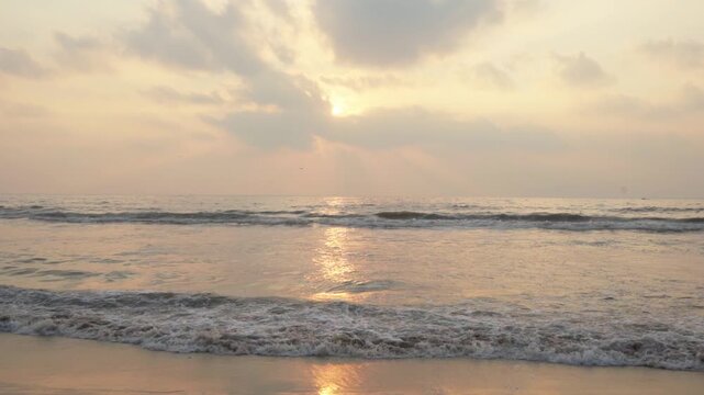 Golden sunbeams shining through morning clouds and reflecting on wet beach sand