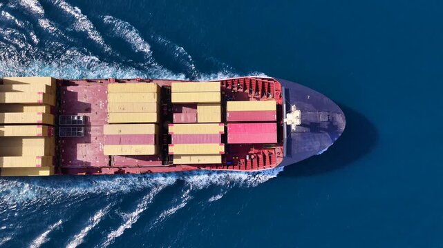 Aerial drone top down cinematic tracking loop video of container ship cruising deep blue open ocean sea