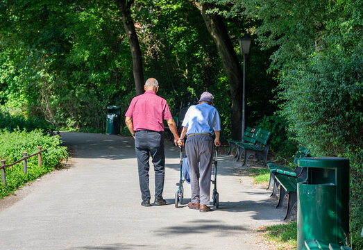 Zwei &auml;ltere M&auml;nner, Senioren gehen entspannt im Park spazieren -  Sohn und Opa mit Rollator