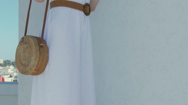 Woman in white dress with woven bag and belt on a sunny day