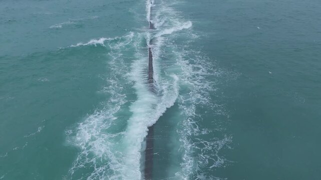 Aerial drone video of waves following the jetty wall to shore