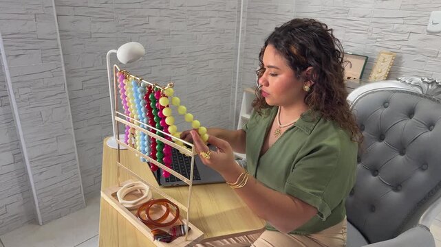 Creative woman designing and making colorful necklaces and bracelets at her home workshop