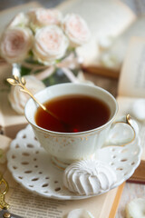 Fototapeta premium A cup of tea, a cake and beautiful and delicate roses on a table with books.