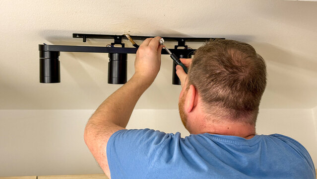 Man installing modern ceiling track lighting in a bright home interior, close-up detail ideal for DIY tutorials, home improvement blogs, social media and editorial use
