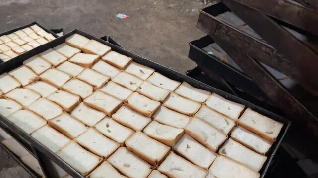 High angle view of many sliced white bread pieces arranged on large metal baking trays in a commercial bakery setting