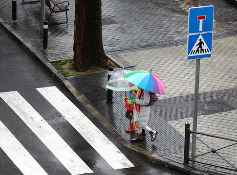 Paraguas de colores alegres en d&iacute;a de lluvia cruzando paso de peatones con se&ntilde;al vial en calle urbana