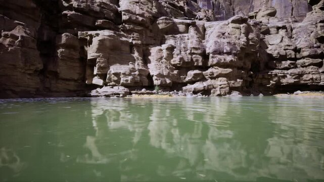 Textured sandstone face reflected in green water, intricate shadows and highlights, vertical strata emphasized, gentle ripples distort mirror image, study