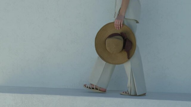 Woman in light clothing holding a straw hat walks on a sunny day