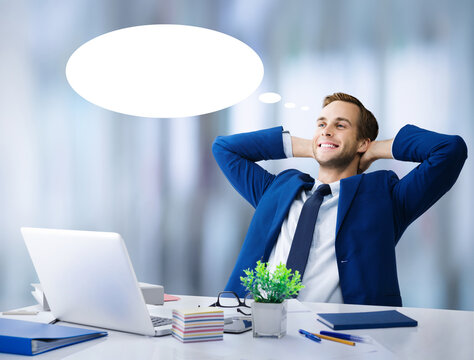 Happy smile relaxing or dreaming businessman with hands behind head. Business man in blue suit with laptop notebook computer at office. White empty think bubble thinkbubble, thought float, free space