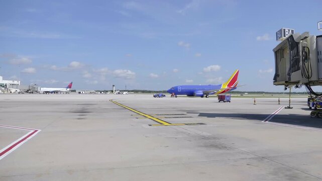 Ground Crew Preparing Blue Airplane At Jet Bridge On Airport Tarmac With Tow Tractor