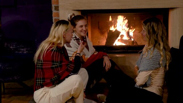 Close friends enjoying a relaxed fireside conversation, sitting comfortably in a warm living room environment with soft lighting and cozy winter lifestyle atmosphere