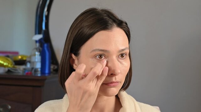 Woman applying concealer to her face using fingers during a home beauty routine. Natural makeup technique, skin correction, and cosmetic application.