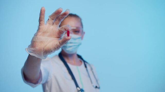 Female doctor wearing a protective mask and gloves holding a new red pill for a revolutionary medical treatment in her hand