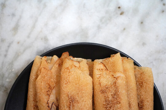Top View of Bengali Patisapta Pitha Rolled Crepes on Black Plate Over Marble