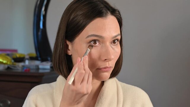 Young woman blending concealer with a brush at home