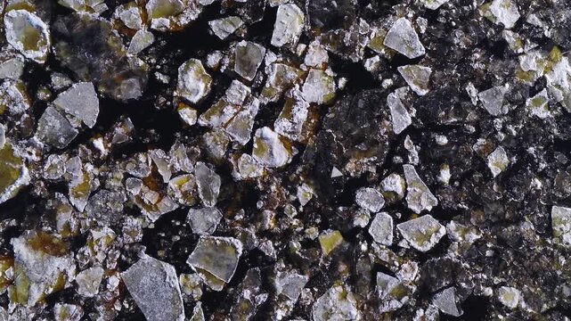 Aerial top down view shows jagged ice floes and black leads drifting near Mangalsala Lighthouse in Riga, Latvia, with snow rims and yellow brown sediment stains.