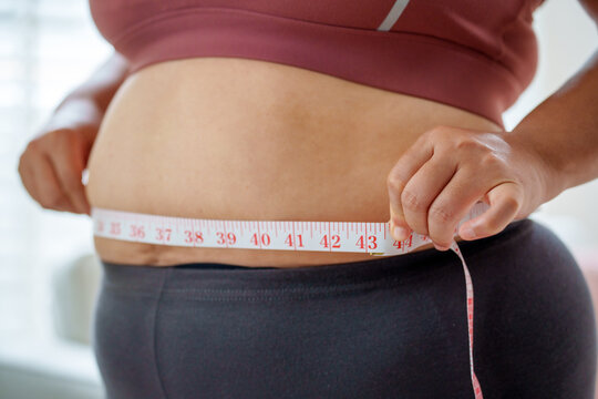 Determined woman checking waist size with measuring tape, Health care and obesity control concept.