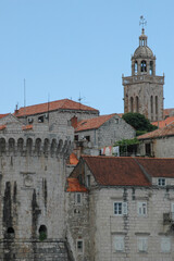 Obraz premium A scenic view of the historic Korcula old town featuring a massive stone fortification tower and the bell tower of St Mark Cathedral rising above red terracotta roofs