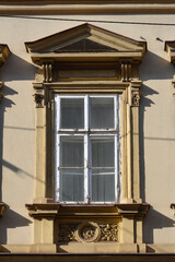 Obraz premium An old white wooden window featuring a decorative stone frame with classical ornaments and a triangular pediment on a beige building wall