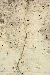 Obraz premium A full frame vertical shot of a weathered beige concrete wall featuring a prominent jagged vertical crack and a porous pitted surface