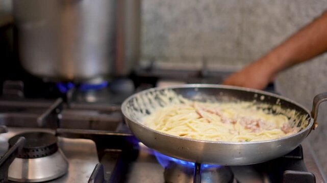 A chef in an Italian restaurant prepares pasta in a large pan
