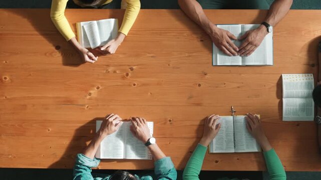 Top view of prayer hold each other support while prays to god at table with bible and cross placed with faith, spirituality and religion. Aerial view of diverse people holding and praying. Symposium.