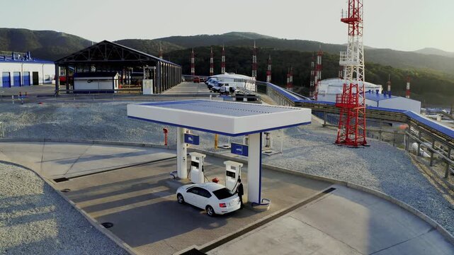 Man fills up his white sedan car with fuel at a gas station 