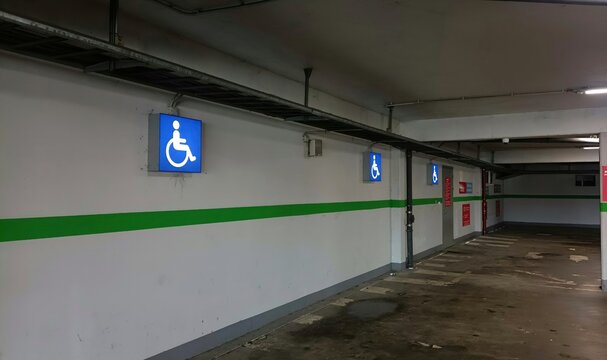 Disabled parking signs in a modern underground garage. Glowing blue wheelchair symbols for accessibility and inclusive urban environment.