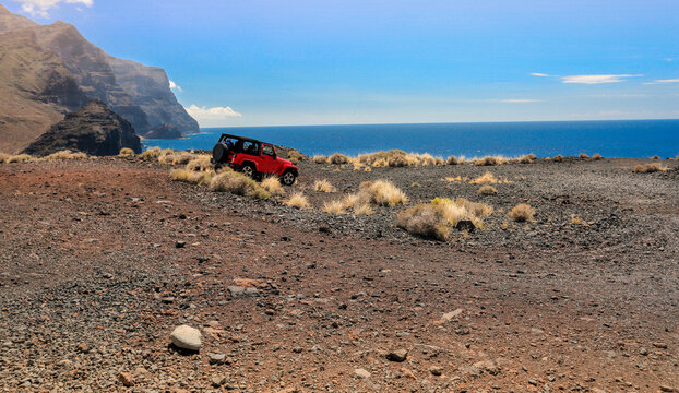 Dramatic coastal landscape featuring rocky cliffs, mountains, dry grasses and the sea under a sunny summer sky. Adventure, exploration and the spirit of traveling into the unknown.