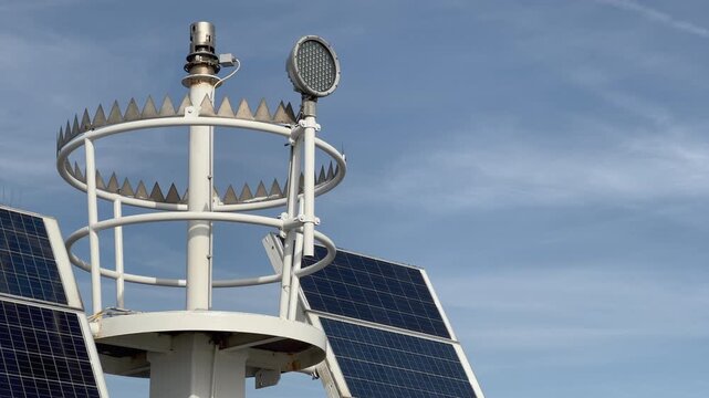 Detailed close-up of weather station anemometer and meteorological sensors mounted on pole with solar panels visible, technical equipment for atmospheric and climate data collection.