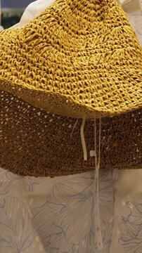 Golden straw hat on hanger near window, styled for resort getaway by visual merchandiser, woven brim detail, evening city lights bokeh, linen garment backdrop, aspirational travel and chic vacation