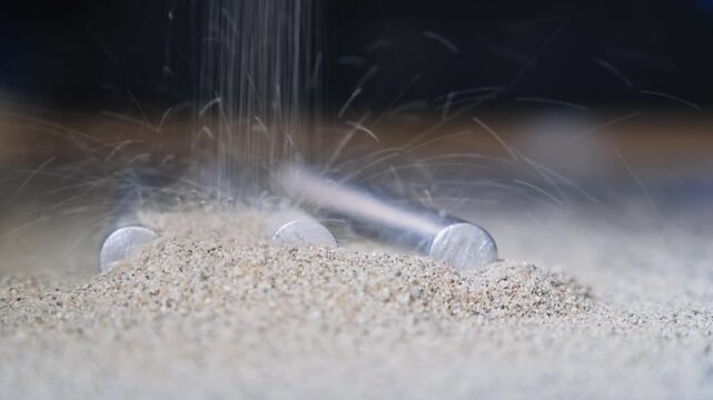 Close up of aluminum rods being gradually covered by loose quartz sand, where their defined shape fades into a more uniform and disordered structure.